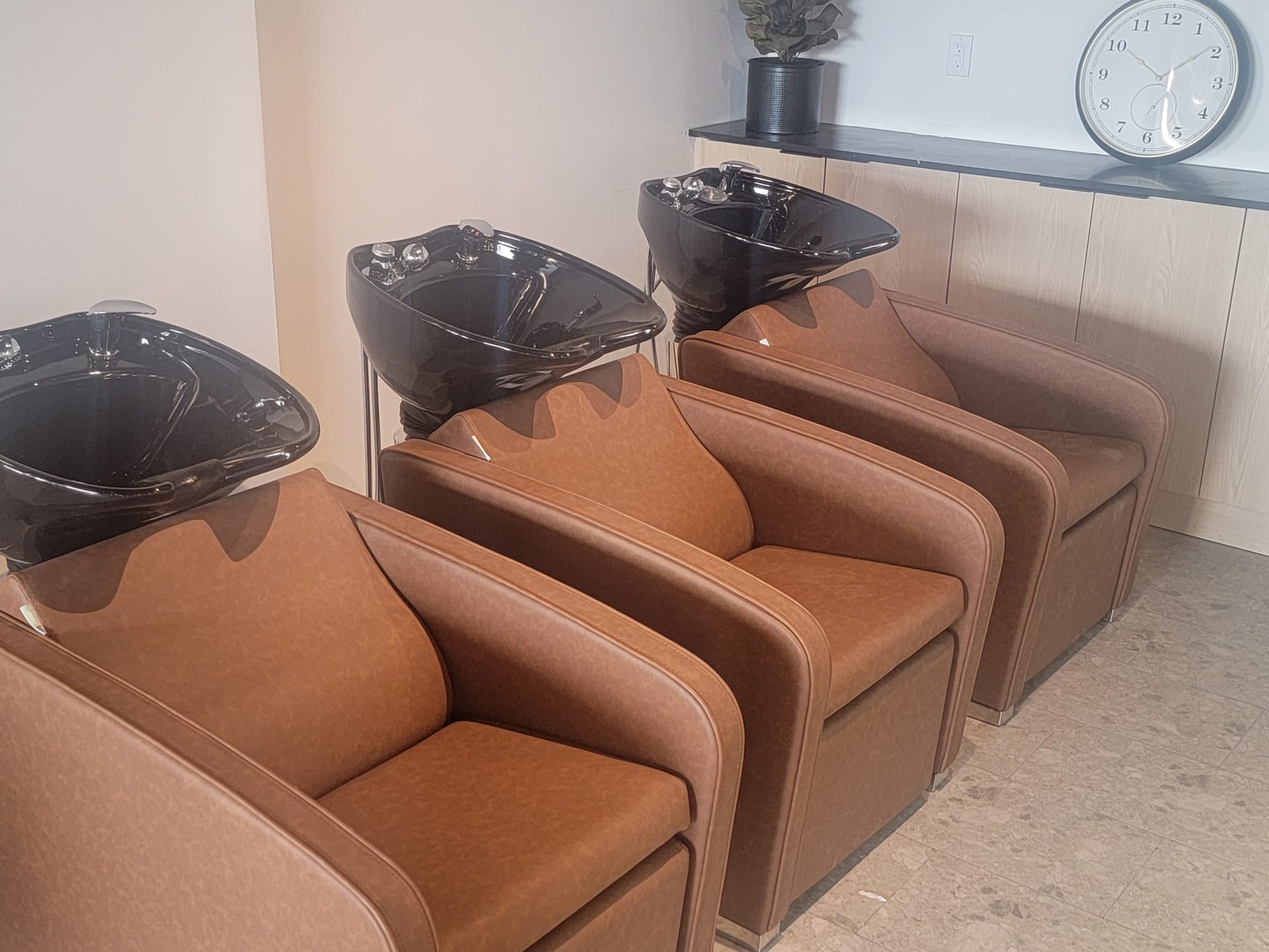 Row of shampoo wash basins with reclining cognac-brown chairs in a bright salon wash area